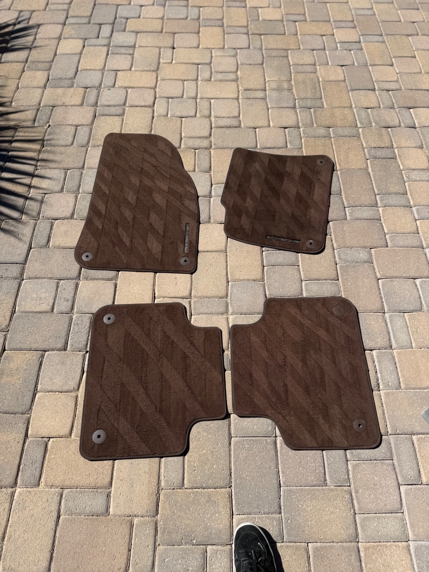 Freshly cleaned Porsche floor mats laid out on a paver driveway